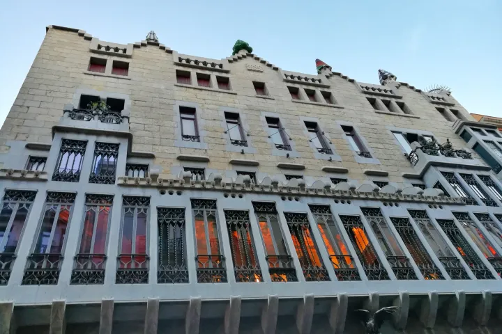 Die Steinfassade des Palau Güell, seine schmiedeeisernen Galerien und die Schornsteine, die über das Dach hinausragen