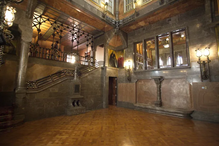 Der zentrale Salon des Palau Güell, ein weitläufiger Raum mit Parkettboden, der zu den Galerien und der Treppe hin offen ist