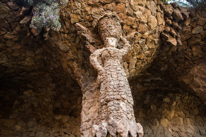 La colonna scolpita a forma di lavandaia, sotto la volta di pietra grezza del portico del Parco Güell