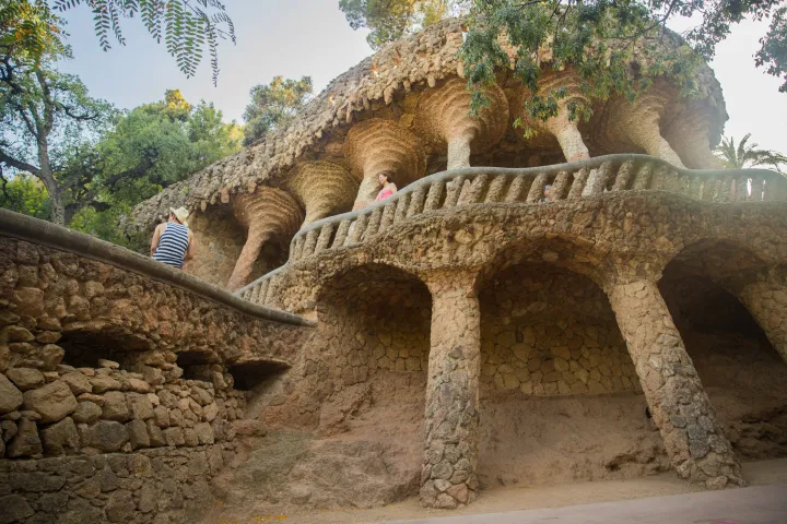 Un viadotto del Parco Güell, il suo arco di pietra grezza e il sentiero fiancheggiato da fioriere