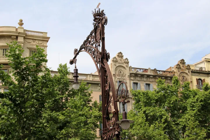 Un banco-farola modernista de hierro forjado y trencadís en el Passeig de Gràcia, frente a las fachadas de la avenida