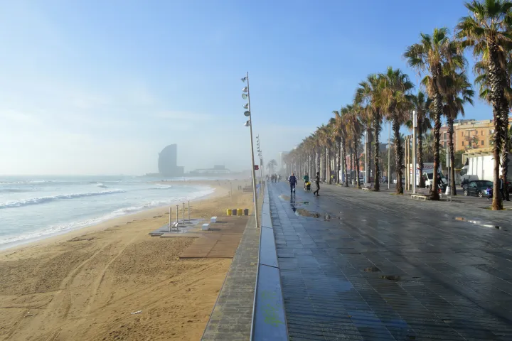 O Passeio Marítimo da Barceloneta, com suas palmeiras, seus passeantes e a praia, o hotel W ao fundo