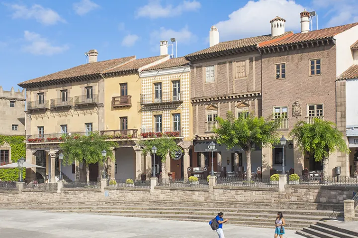 The facades and arcades of the Plaça Major in Poble Espanyol under a blue sky