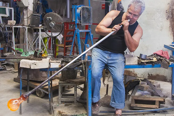 An artisan blows a piece of still glowing glass in his workshop at Poble Espanyol