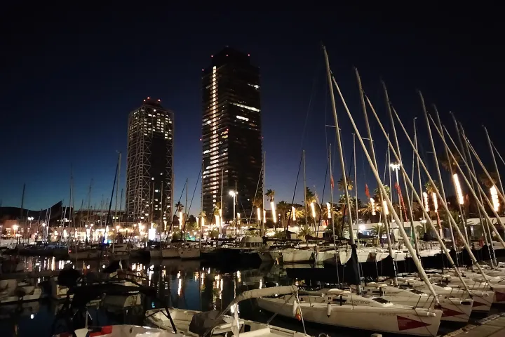 Os cais reformados do Moll de Gregal à noite, os mastros dos veleiros e as torres do Hotel Arts e da Torre Mapfre iluminadas
