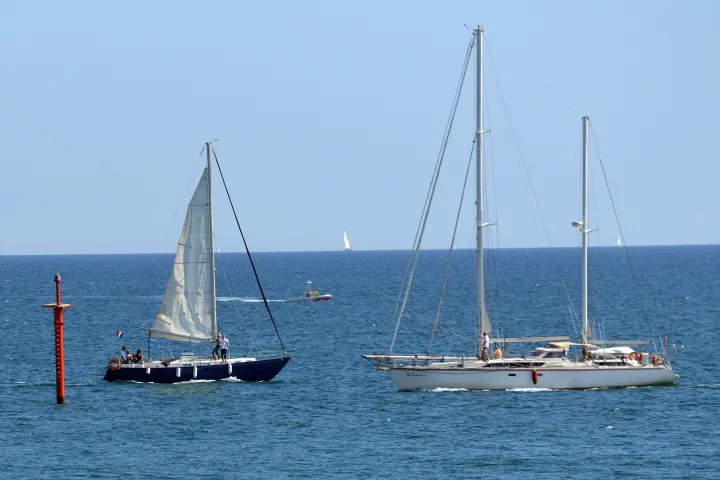 Dois veleiros navegando ao largo do Porto Olímpico, sobre um mar azul