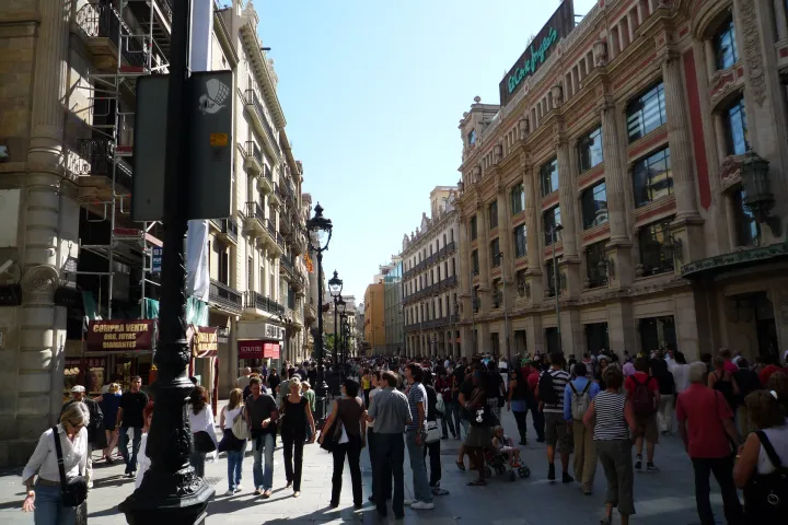 Transeúntes en la avenida peatonal Portal de l’Àngel, frente a los escaparates y el antiguo edificio de El Corte Inglés.