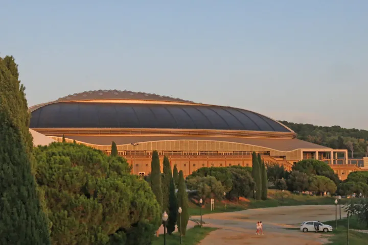 Il lungo tetto curvo e il profilo molto basso del Palau Sant Jordi, dietro i pini e i cipressi di Montjuïc