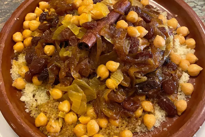 Couscous topped with chickpeas, raisins, and vegetables in an earthenware dish.