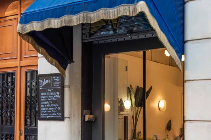 Entrance of the bar under a blue awning, featuring a chalkboard and lights inside.