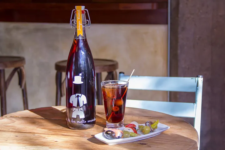 Flasche Wermut, Glas und kleiner Teller mit Oliven auf einem Tisch.