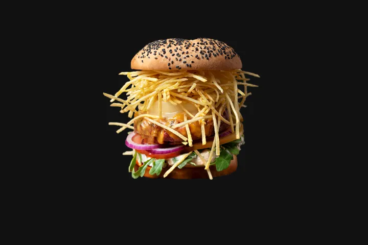 Burger with a bun topped with black seeds, garnished with cheese and thin potato slices.
