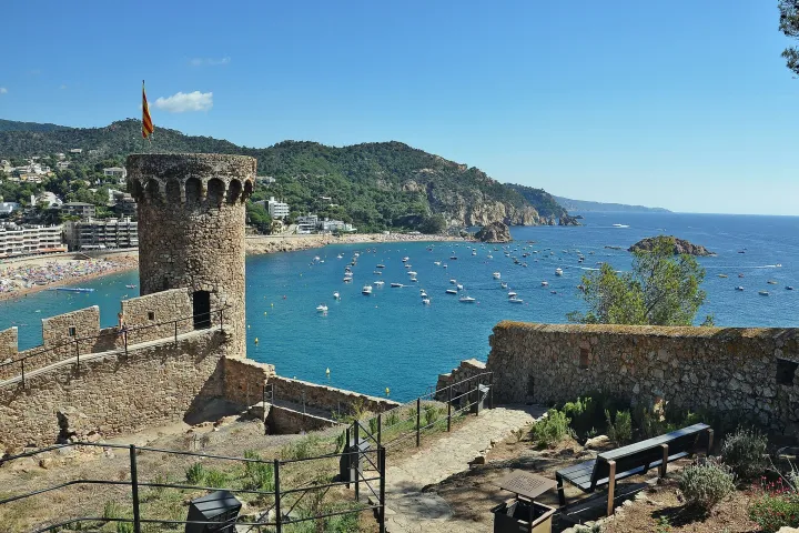 Ein Turm und die Mauern der Vila Vella überragen die Bucht von Tossa de Mar, wo Boote vor Anker liegen.