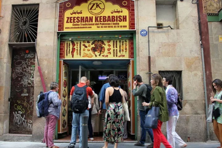 Passersby in front of the entrance to Zeeshan Kebabish, under its red and yellow sign.