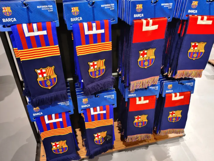 Blaugrana-Schals mit dem Wappen des FC Barcelona, die an einem Ständer hängen.