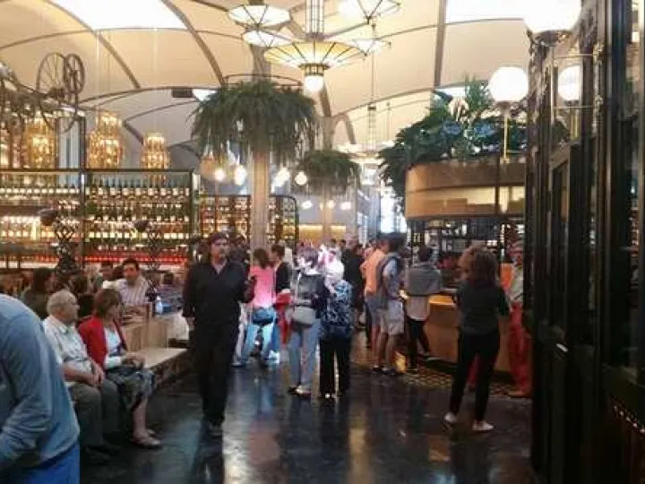 Clients dans l'allée centrale d'El Nacional, entre les comptoirs, sous de grands luminaires et des plantes suspendues.
