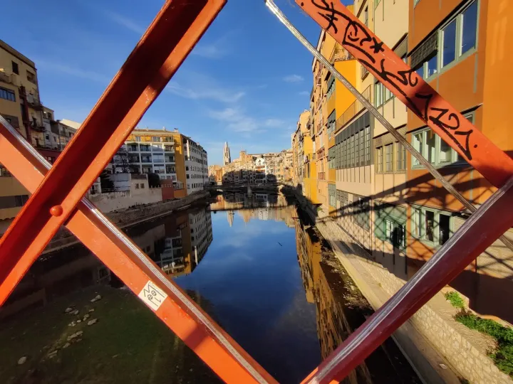 Die bunten Häuser spiegeln sich im Onyar wider, gesehen durch die rote Struktur der Eiffel-Brücke.