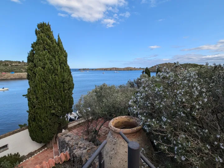 A cypress, a large jar, and the garden walls frame a view of the bay of Portlligat.