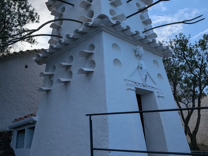 A white tower topped with an egg features protruding shapes and long dark branches under the blue sky.