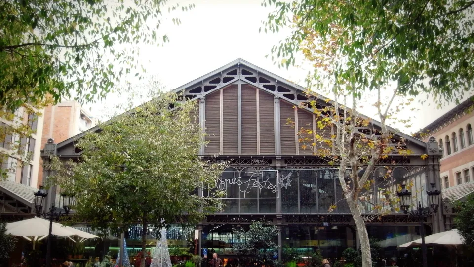 Die Eisen- und Glashalle des Mercat de la Concepció, seine Terrassen und Bäume entlang der Straße