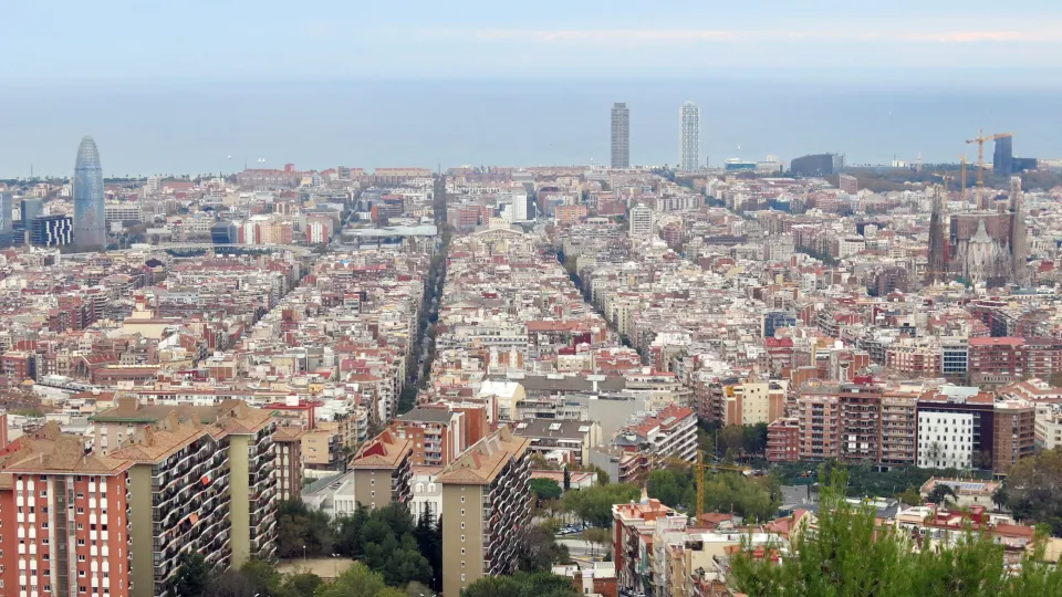 O tabuleiro do Eixample visto do Turó de la Rovira, com suas ruas retas se estendendo em direção ao mar, a Sagrada Família e a Torre Glòries