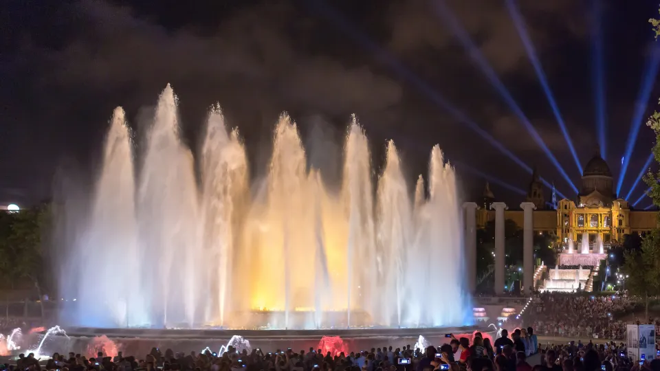 The Magic Fountain lit up at night in front of the Palau Nacional and its light beams, with the crowd in the foreground