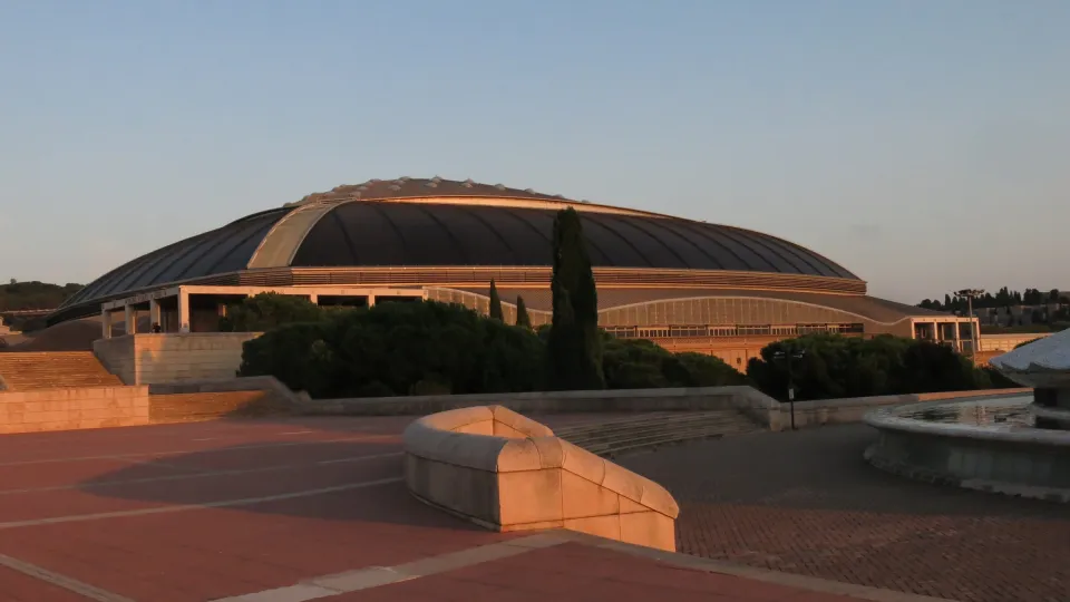 Il Palau Sant Jordi e il suo ampio tetto curvo visti dall'esplanade dell'Anella Olímpica, al tramonto