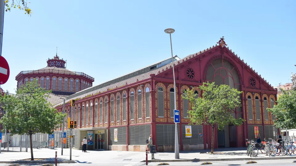 Der Mercat de Sant Antoni und seine rote Gusseisenhalle, gesehen von der Straßenecke unter blauem Himmel