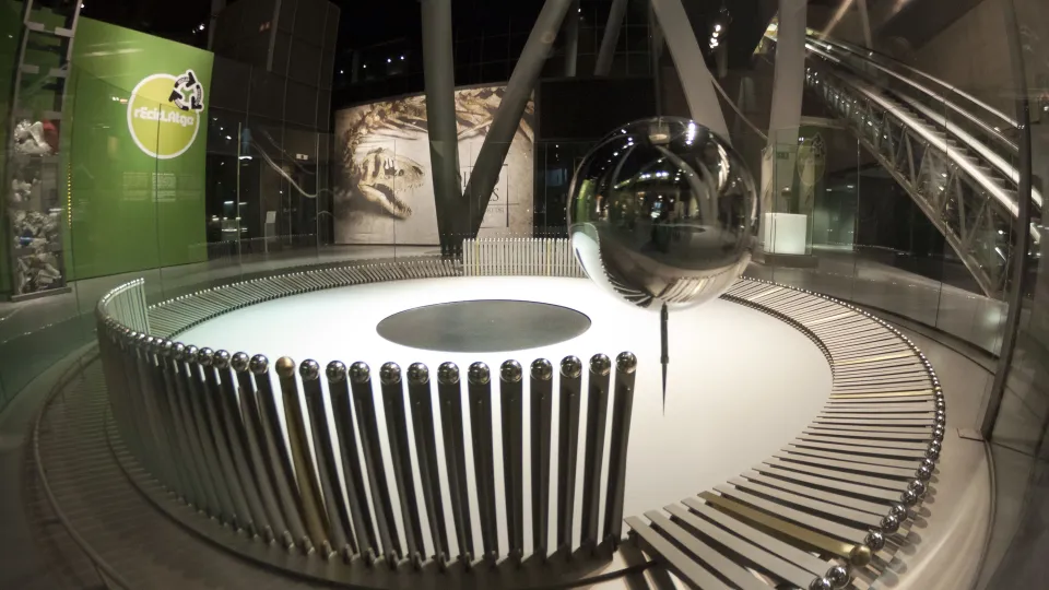 La sphère métallique du pendule de Foucault suspendue au-dessus de son cercle de quilles, dans le hall du musée